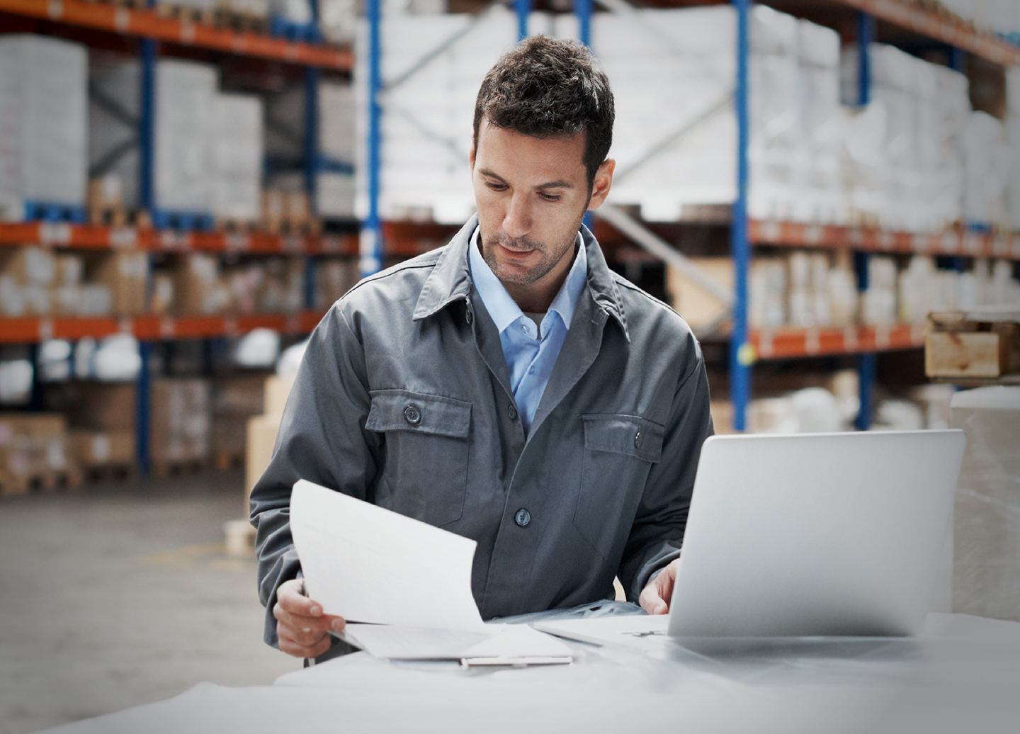 Man at desk looking at paperwork, in a warehouse.