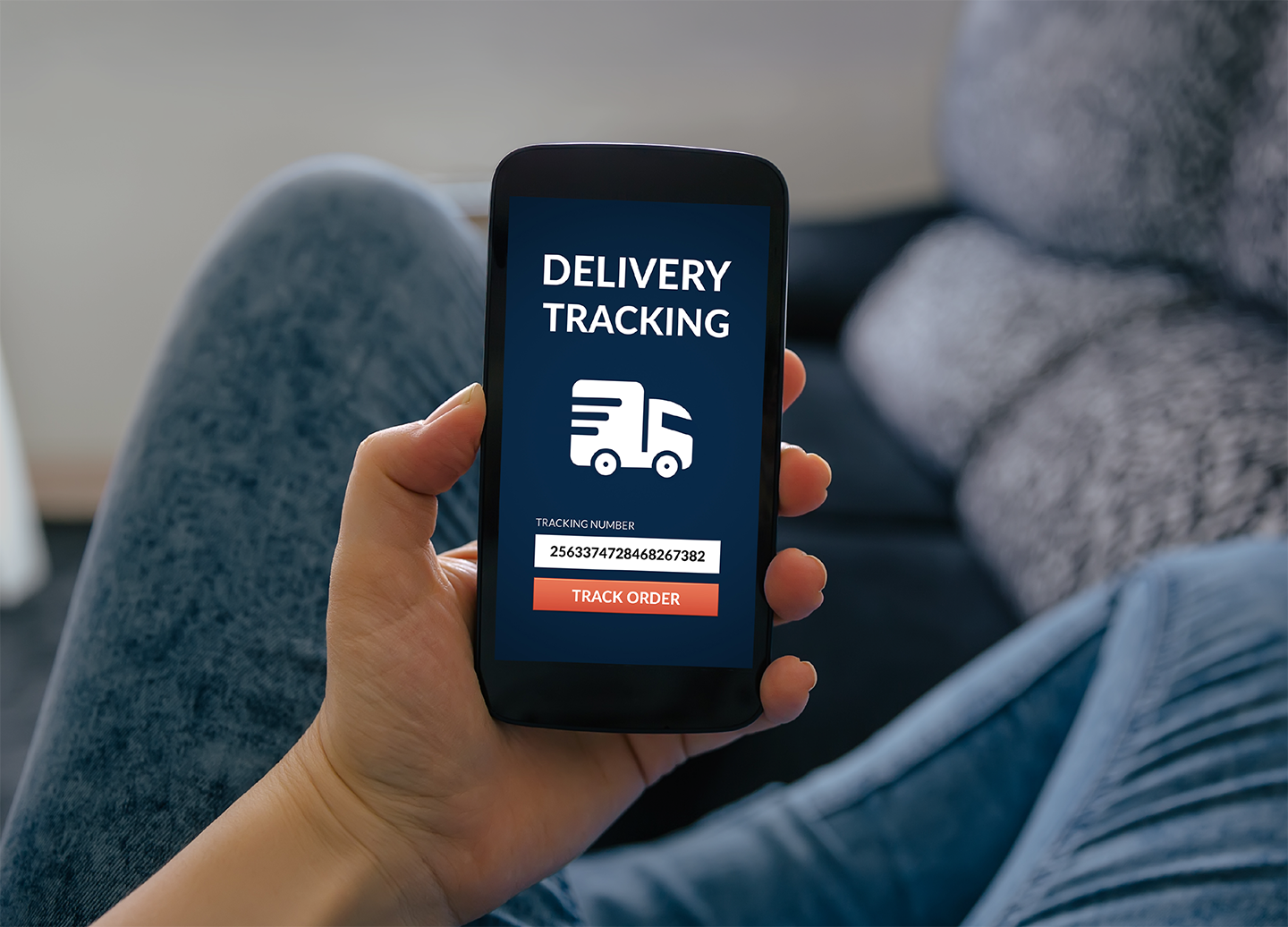 Hand holding a smartphone displaying a delivery tracking screen with a truck icon and a tracking number field