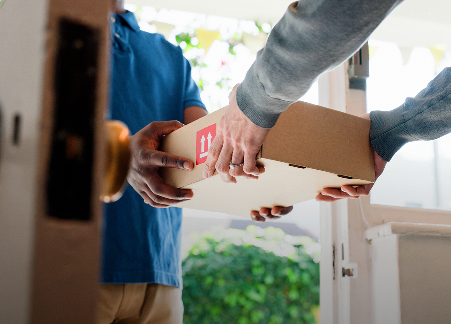 Delivery handoff: two people exchange a small cardboard box at a doorway (labelled handling arrows).